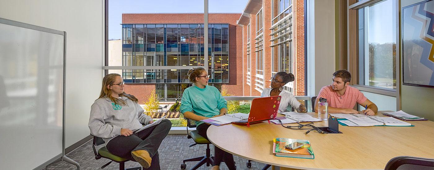 4 students sit in a study room in the Gira Center and work on a group project